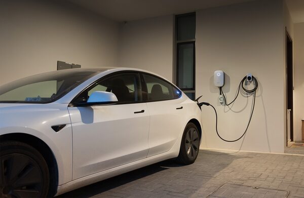A white electric car charging from a wall-mounted EV charger in a home garage