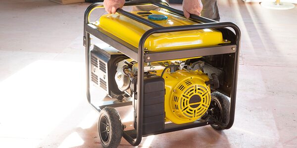 A person carrying a yellow portable petrol generator with wheels and a black frame