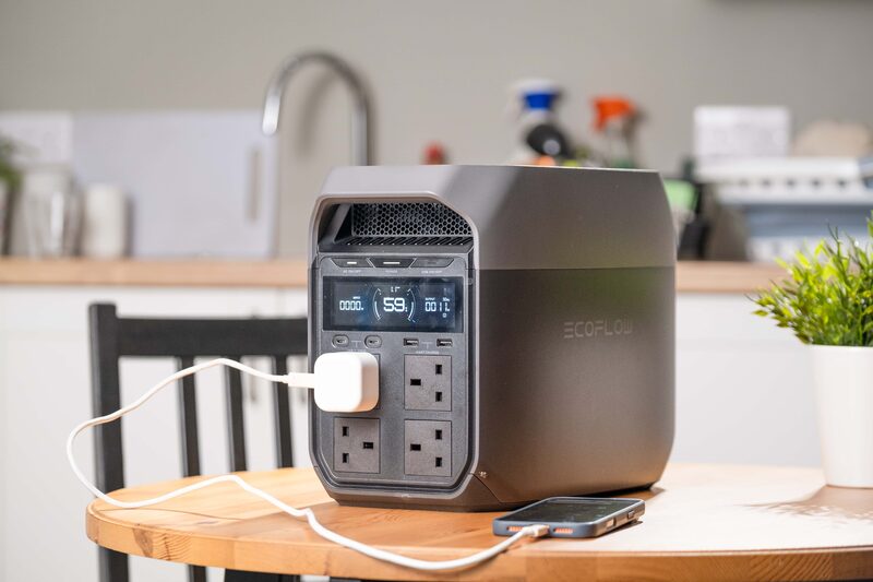 An EcoFlow portable power station with UK plug sockets and display sitting on a kitchen table, charging a phone