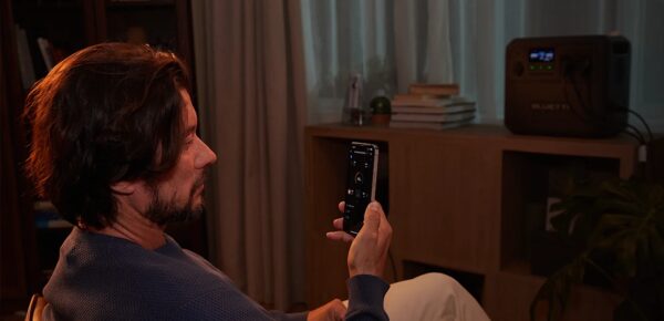 A man sitting in a dim living room controlling a BLUETTI portable power station with a smartphone app
