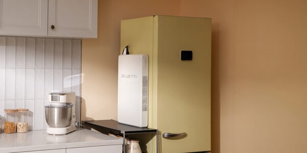 A white BLUETTI portable power station standing on a shelf beside a retro green fridge in a kitchen