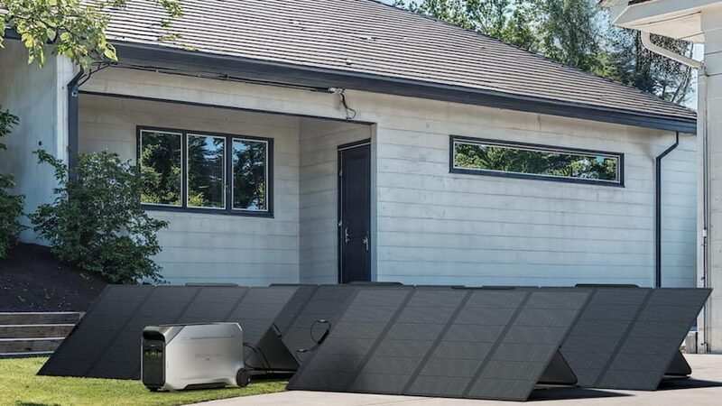 An EcoFlow DELTA Pro 3 portable power station connected to several folding solar panels laid out on the ground outside a modern house