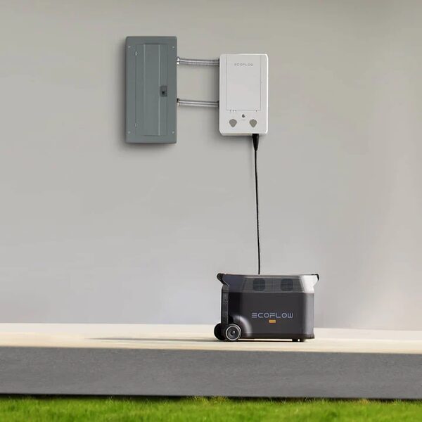 An EcoFlow portable power station connected by cable to a wall-mounted transfer switch and consumer unit outside a home