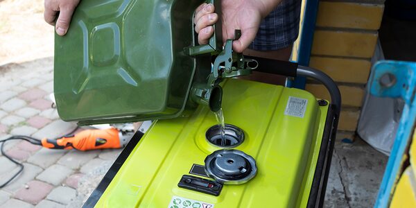 A person pouring petrol from a green jerry can into the fuel tank of a yellow portable generator