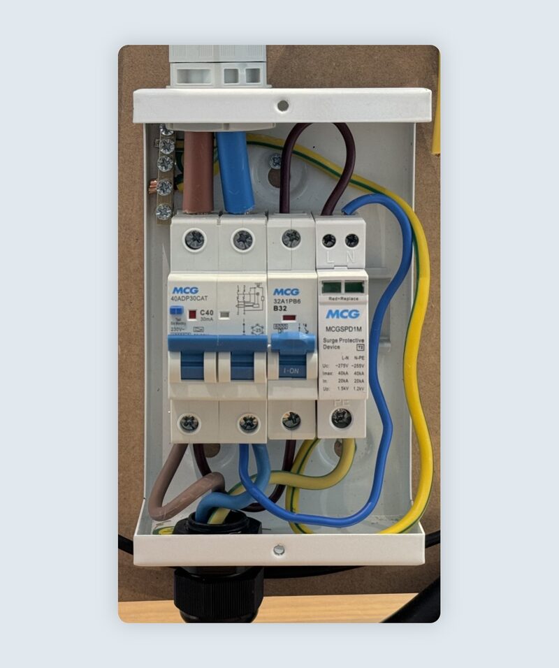 A small consumer unit with MCG circuit breakers, an RCBO and a surge protection device wired with blue, brown and yellow-green cables