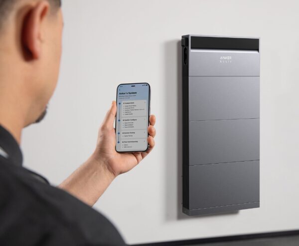 A man using a smartphone app to control a wall-mounted Anker SOLIX home battery