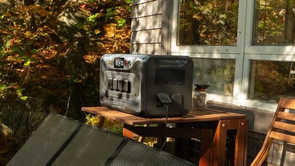 A BLUETTI portable power station on a wooden table outside a cabin, plugged in beside a portable solar panel