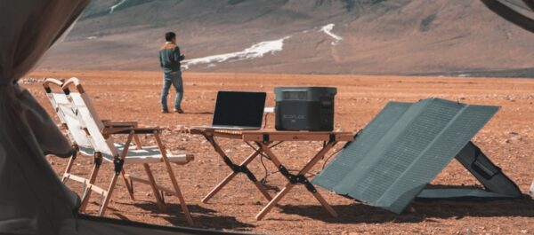 A portable EcoFlow power station charging a laptop beside a folding solar panel at a desert campsite