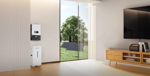 A LuxpowerTek wall-mounted hybrid inverter and battery storage unit installed in a modern living room beside a glass door with solar panels visible outside