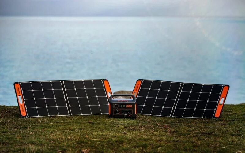 Two Jackery portable folding solar panels propped on grass beside a Jackery power station, with a lake in the background