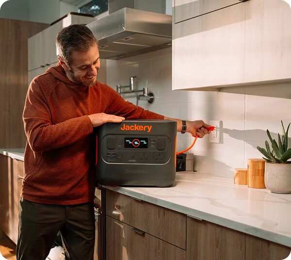 A man plugging a Jackery Explorer portable power station into a kitchen wall socket