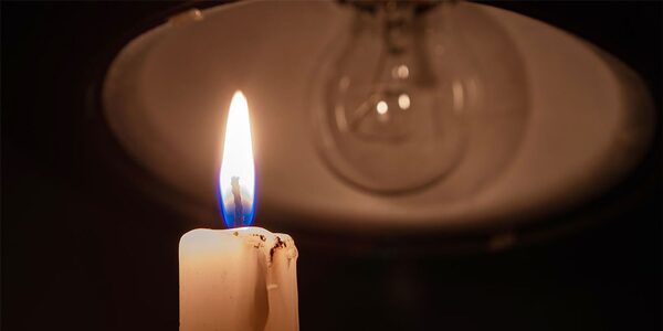A lit candle in front of an unlit light bulb during a power cut