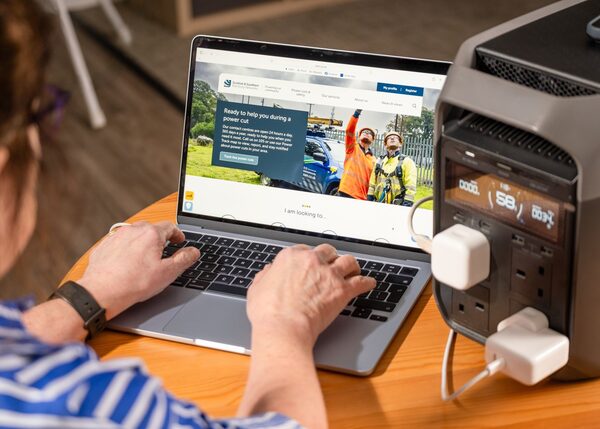 A woman using a laptop showing the SSEN website, powered by a portable battery power station with plugs attached