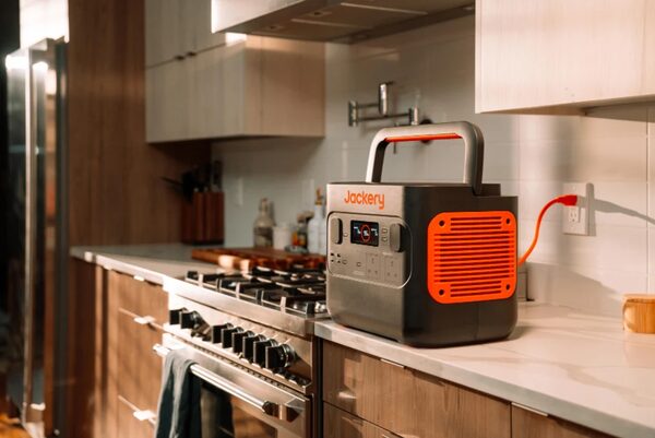 A Jackery portable power station plugged into a wall socket on a kitchen worktop