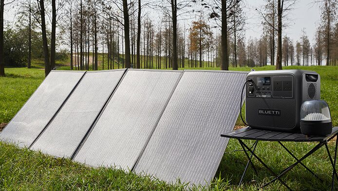 A Jackery portable power station connected to a folding solar panel set up on a grassy lawn