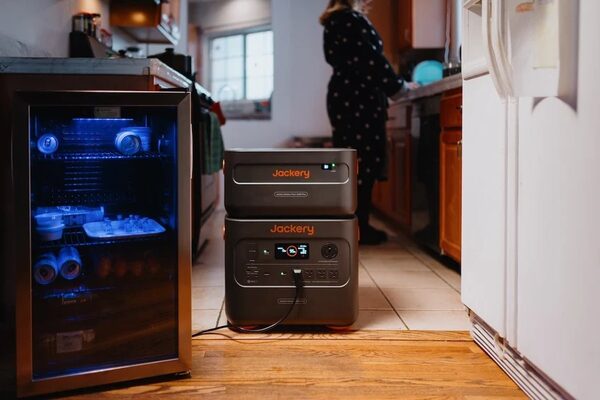 A Jackery portable power station with a stacked battery unit powering a mini fridge in a home kitchen