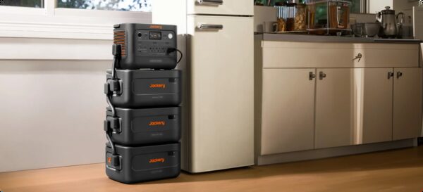 A Jackery HomePower portable power station stacked with three expansion battery units on a kitchen floor next to a fridge