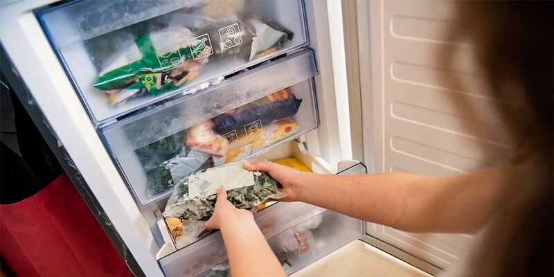 A person placing a bag of frozen vegetables into the drawer of an open chest-style freezer filled with frozen food