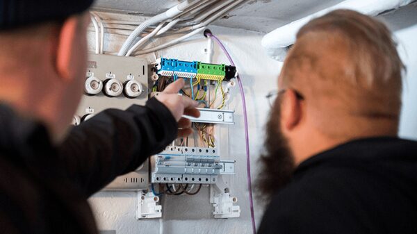 Two electricians inspecting and pointing at a domestic fuse box with wiring and circuit breakers