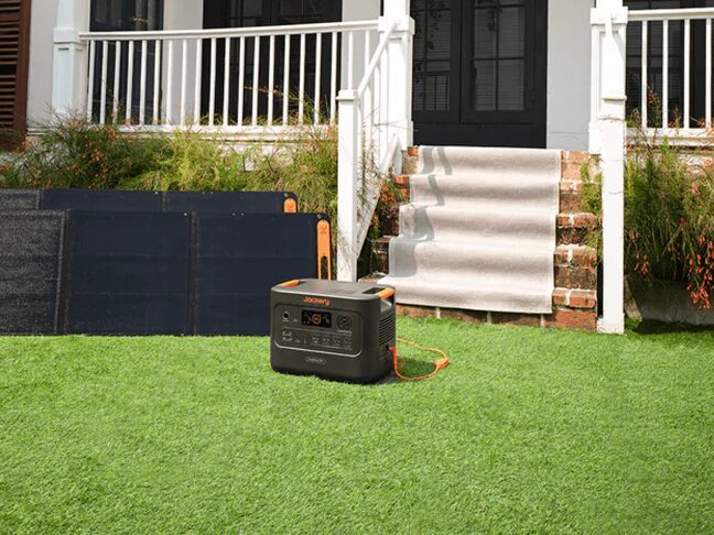 A Jackery portable power station on a lawn outside a house, connected to folding solar panels