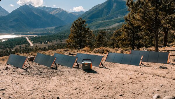 Several Jackery portable folding solar panels propped on a hillside charging a portable power station, with mountains behind