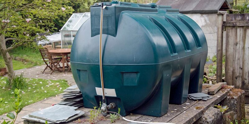 A large green domestic heating oil tank installed in a garden with a fill hose attached
