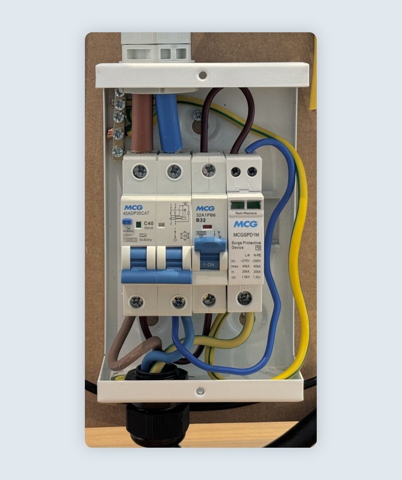 An open consumer unit with MCG circuit breakers, an RCBO and a surge protective device wired with blue, brown and yellow-green cables