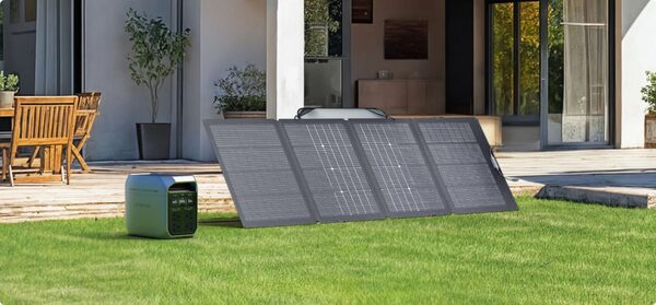 An EcoFlow portable power station with a foldable solar panel array set up on a lawn outside a modern house