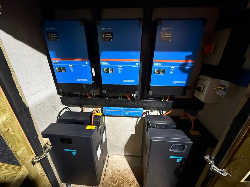 Three Victron MultiPlus-II inverters mounted on a wall above black Fogstar home battery units in a small utility cupboard
