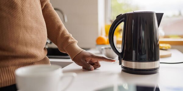 A person switching on a black electric kettle on a kitchen worktop