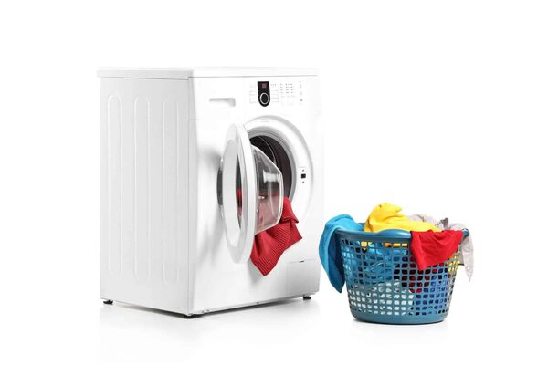 A white washing machine with its door open next to a blue laundry basket full of clothes on a white background