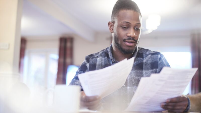 A man at home reviewing paper bills and documents at a table