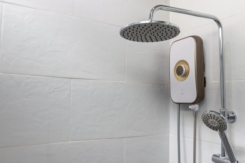 An electric shower unit with rainfall head and handheld shower mounted on white tiled bathroom wall