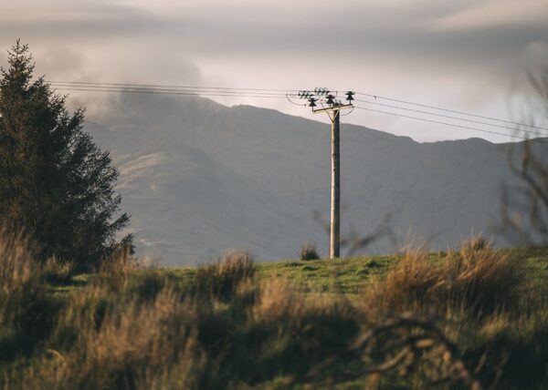 A wooden electricity distribution pole with overhead power lines crossing a grassy hillside in front of misty mountains in the Scottish Highlands