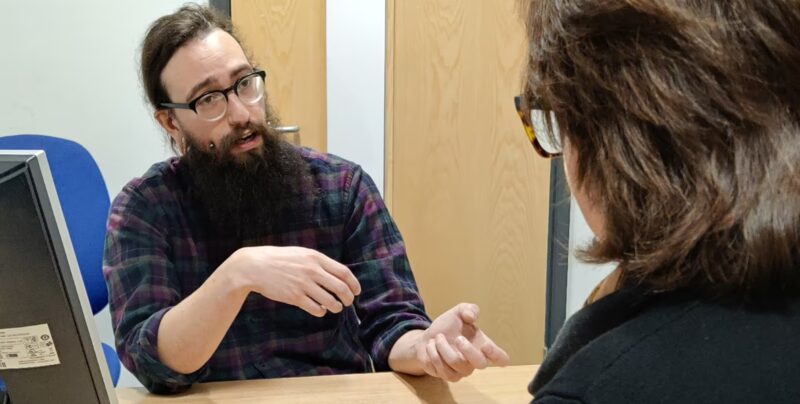 A bearded adviser in glasses talking with a woman across a desk in an office advice session