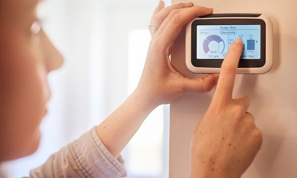 A woman touching a wall-mounted smart energy monitor displaying electricity usage