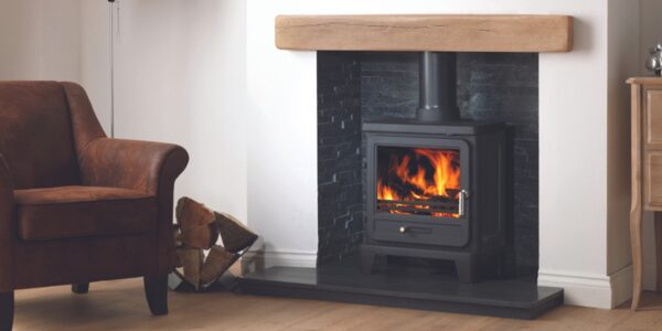 A black wood-burning stove with flames burning, installed in a fireplace with a slate hearth and wooden mantel in a living room