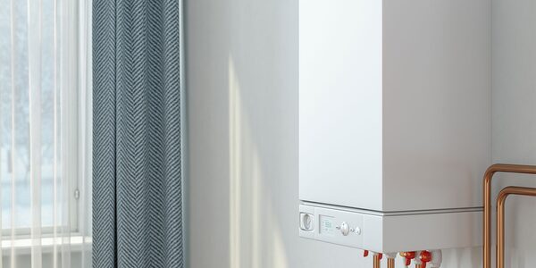 A white wall-mounted combi boiler with copper pipes next to a curtained window in a home