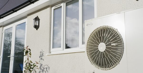 A Grant air source heat pump installed on the exterior wall of a house beside a window and lantern light