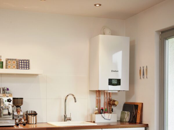 A white Vaillant wall-mounted gas boiler installed above copper pipework in a kitchen corner