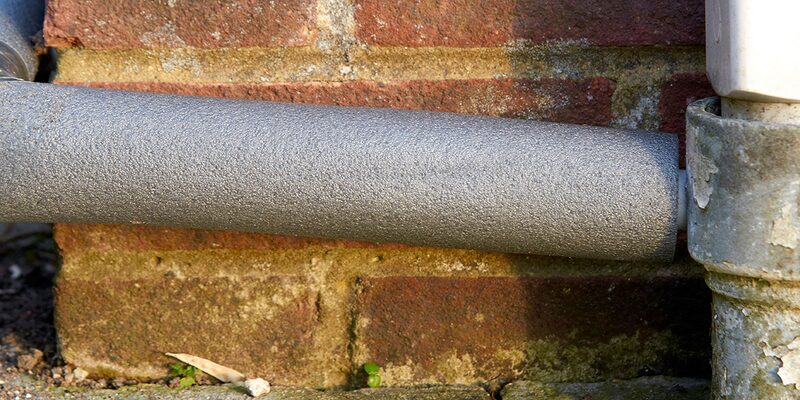 A lagged grey condensate pipe running along an exterior brick wall of a house