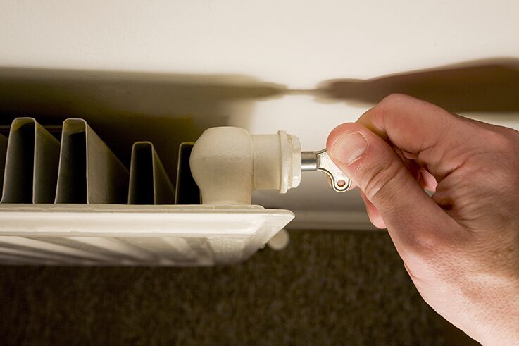 A hand using a bleed key to bleed a white household radiator
