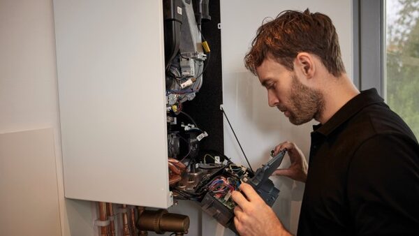 An engineer working on the open internal components of a wall-mounted gas boiler