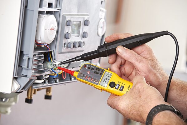 An engineer using a Fluke voltage tester on the wiring of an Alpha wall-mounted gas boiler