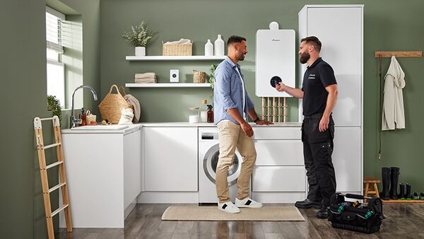 A Worcester Bosch wall-mounted boiler in a utility room with an engineer talking to a householder