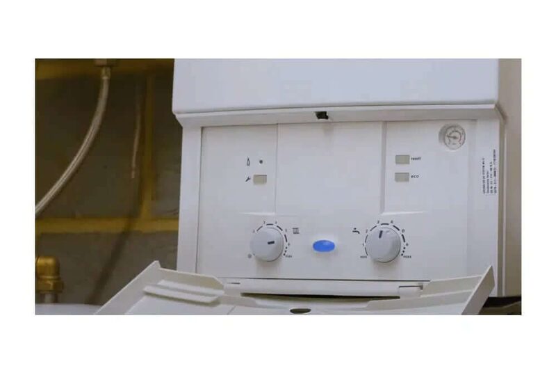 Close-up of a white wall-mounted gas boiler with its control panel flap open, showing two adjustment dials and a pressure gauge