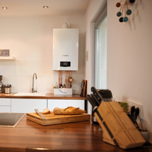 A white Vaillant wall-mounted boiler installed above a kitchen counter with copper pipework, a sink and kitchen items below.