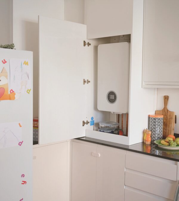 A white wall-mounted combi boiler installed inside an open kitchen cupboard