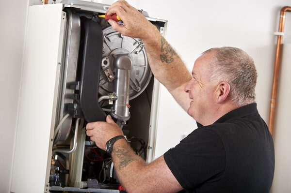 A heating engineer servicing the inside of a wall-mounted gas boiler with a screwdriver