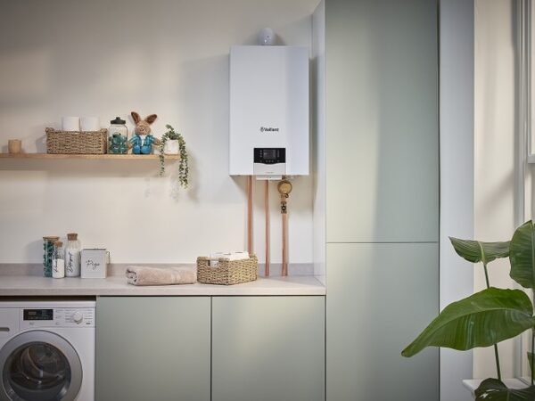 A white Vaillant wall-mounted combi boiler with copper pipework installed in a utility room above a worktop next to a washing machine